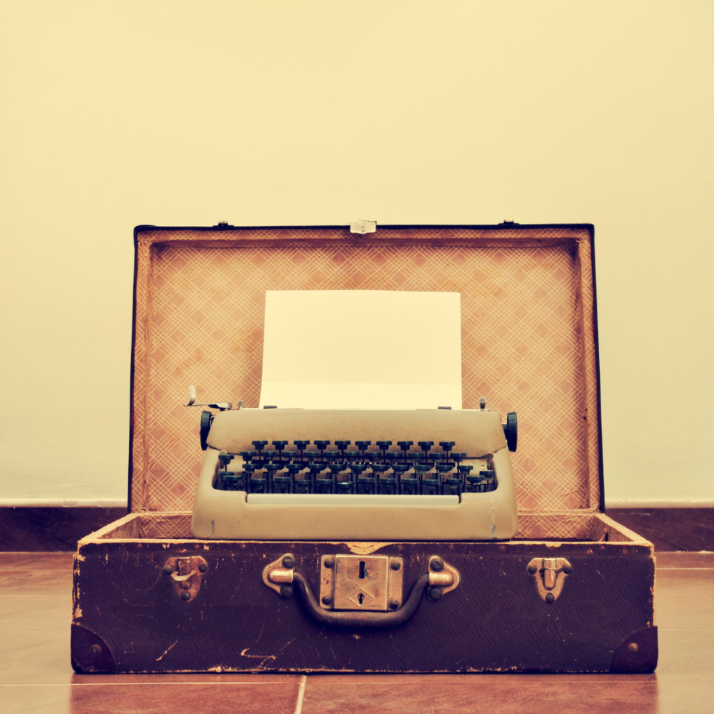 Sepia toned vintage beige typewriter in small open vintage brown leather suitcase
